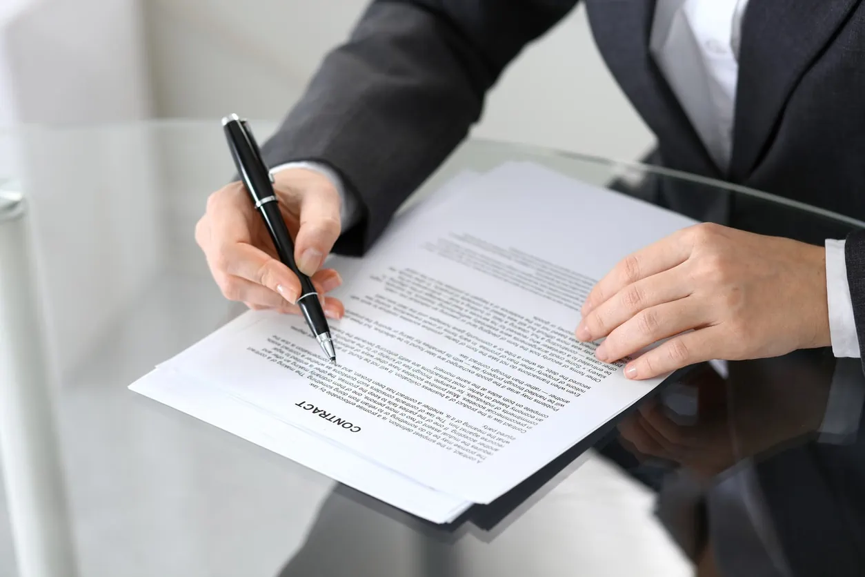 A person in a suit holding a pen over a document that reads "Contract."