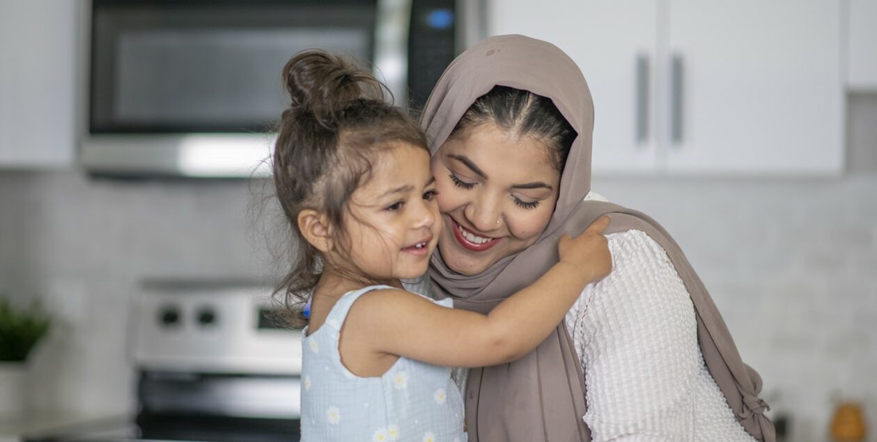 A woman in a headscarf smiling and embracing a toddler.
