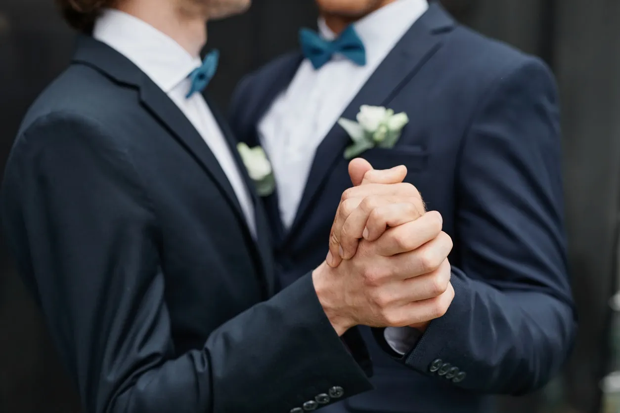 Two men in wedding tuxedos holding hands.
